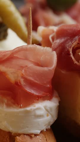 Tapas Spanish pinchos with jamon iberico and goat cheese on bread, Basque pintxo with cured ham and prosciutto slice, traditional bar appetizer vertical close up