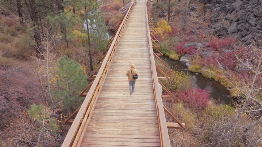 Aerial view of a man walking across a wooden bridge over the Susan River on the Bizz Johnson Trail in Lassen County, California, on an overcast autumn day.
