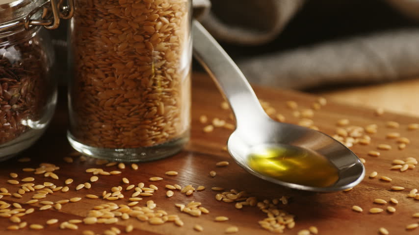 Linseed oil pouring into spoon, flaxseed oil with flax seeds on wooden table, healthy organic omega 3 superfood oil macro close up