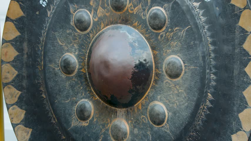 A visitor strikes a large bronze Buddhist gong with a padded mallet in Bangkok.
