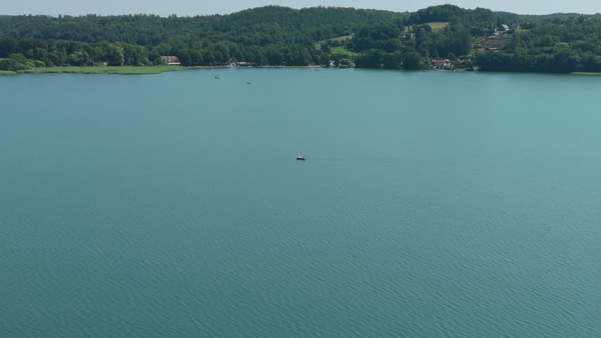 Wide shot of a tranquil blue lake with a single small boat surrounded by lush green forests