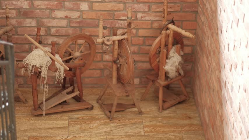 Three vintage wooden spinning wheels with natural wool displayed against a rustic brick wall