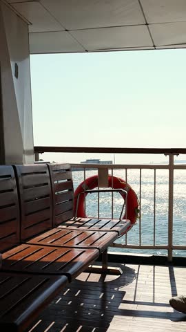 Wooden bench aboard ferry in Istanbul, Turkey, with lifebuoys, blue Bosphorus water and distant city skyline under a clear sunny sky. Travel and tourism concept. Boat moving slowly, vertical shot