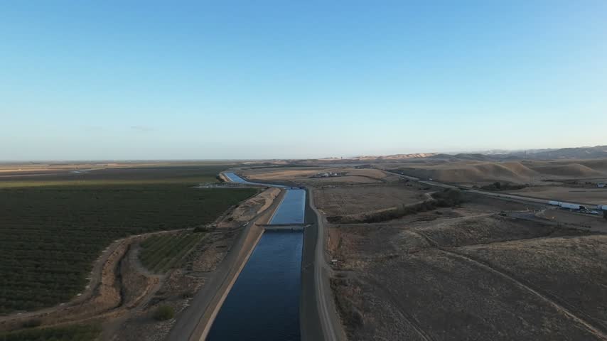 Aerial drone view flying forward over the California Aqueduct, an important water system supplying agriculture and cities, as it winds through the arid landscape of the San Joaquin Valley