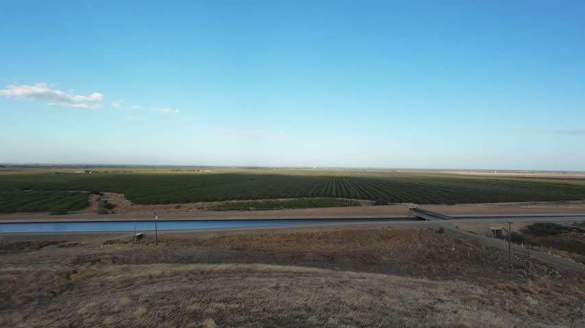 Aerial view flying over the California Aqueduct, a crucial water system irrigating the vast agricultural farmlands of the San Joaquin Valley under a clear blue sky