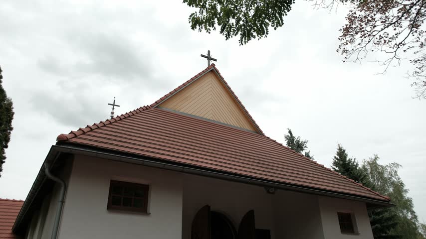 Exterior view of a small white chapel with a red tiled roof and a wooden gable