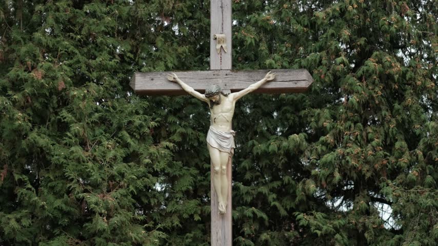 A wooden crucifix with the figure of Jesus Christ outdoors against a background of green trees