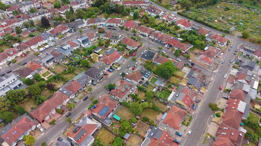 Redbridge London residential crescent seen from above as a forward moving drone shot, showing suburban homes, parked cars, tree lined streets and back gardens in summer.