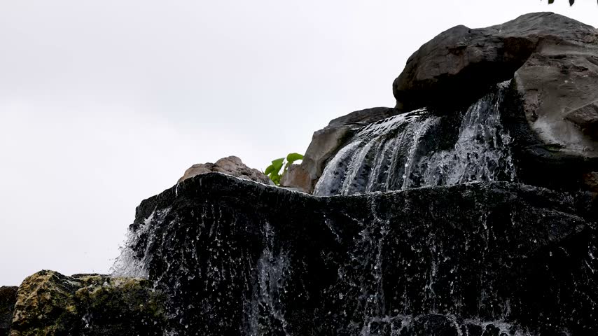 Water cascades down dark rockery tiers of an ornamental garden waterfall in Bangkok, Thailand.