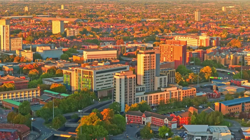 Coventry tower blocks and red rooftops stretching across the city in golden hour light in the West Midlands, England, aerial