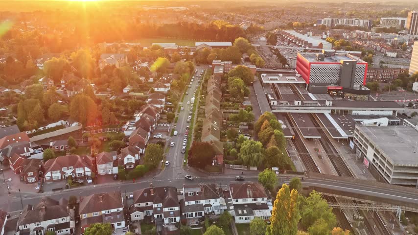 Coventry railway station tracks, platforms and car park beside tree lined streets under a setting sun in Coventry, West Midlands, England, drone forward flyover