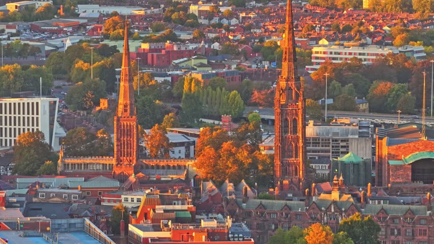 Spires of Coventry Cathedral (ruins of St Michael) and Holy Trinity Church rising above the city centre at golden hour in Coventry, West Midlands, aerial
