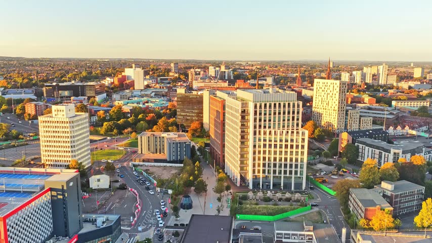 Coventry city centre towers, rooftops and streets glowing at golden hour near the railway station in the West Midlands, England, drone ascent