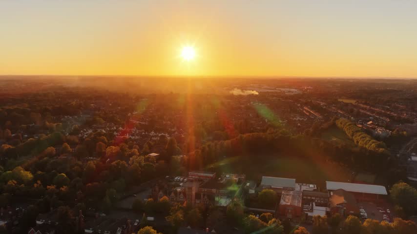 Sun setting with rays over the rooftops and trees of Coventry in the West Midlands, England, aerial