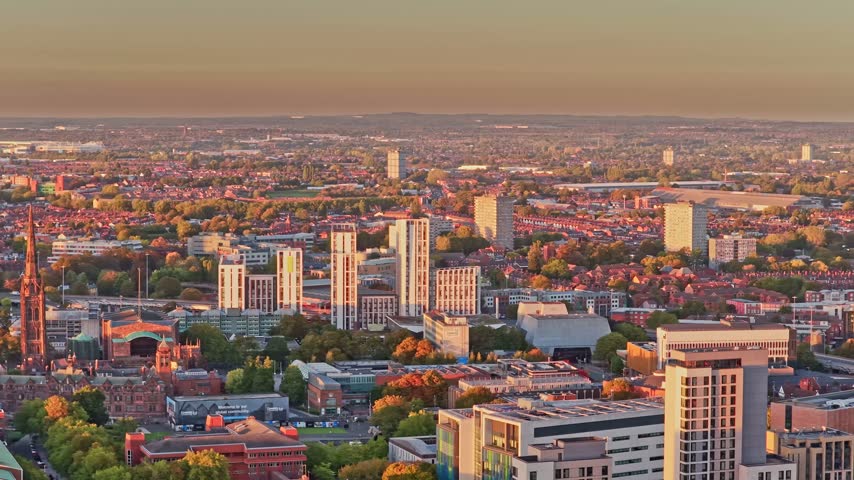 Coventry skyline of tower blocks, office buildings and rooftops in soft evening light in the West Midlands, England, drone lateral slide right