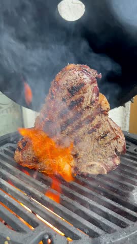 T-Bone Steak Sizzling on a Hot Barbecue Grill with Flames and Rising Smoke