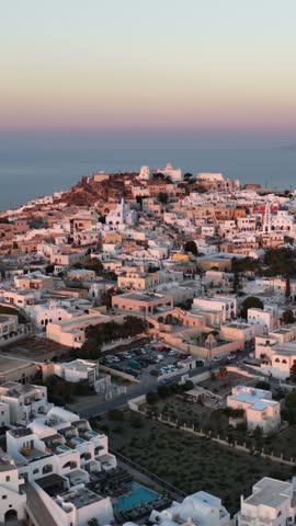 Traditional white houses cover the hillside of Pyrgos in Santorini as dusk arrives over the sea