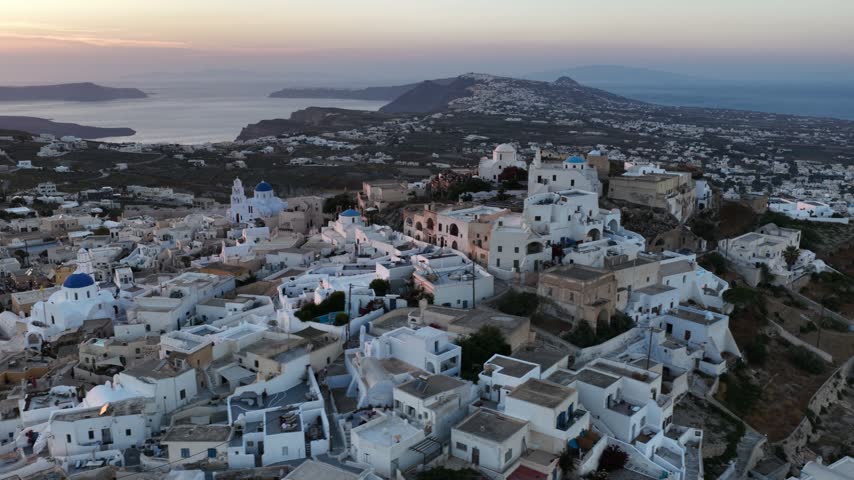 Sun sets over white houses and blue domes of Pyrgos village in Santorini Greece