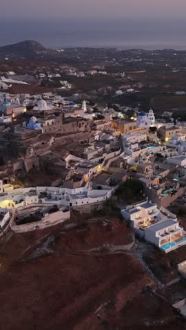 High angle view looking down at the illuminated buildings of Pyrgos in Santorini as evening approaches over Greece