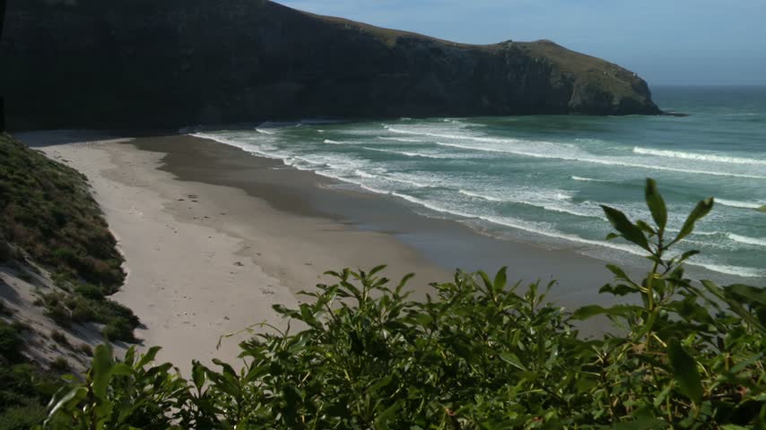 Ocean Waves Crashing Onto a Sandy Shore, Framed by Coastal Hills, Along the Catlins Coast in Otago, New Zealand. wide shot