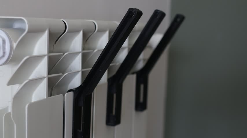 Close-up of hands hanging warm knitted winter clothes and accessories on a home radiator.