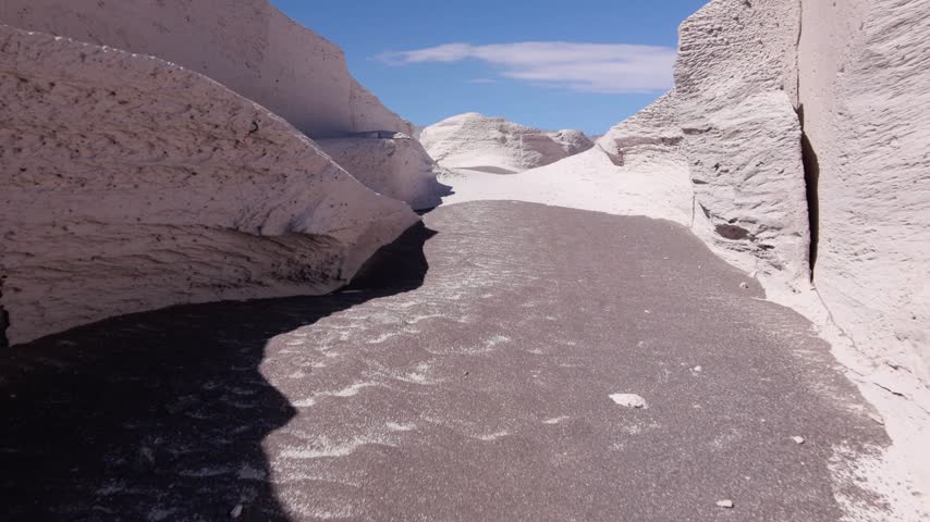 A narrow dark-sand passage winds between tall pale pumice walls; the camera advances through the corridor, showing a route for highland exploration.