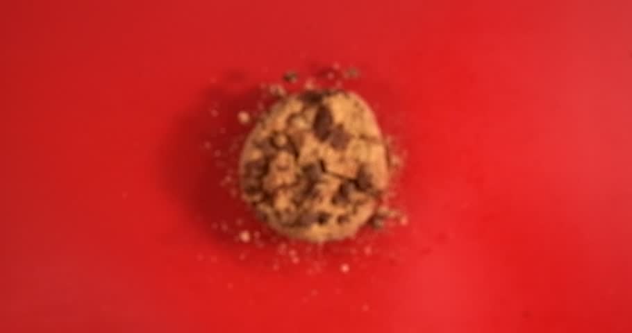 Chocolate chip cookie falling with crunchy crumbs on red background in slow motion