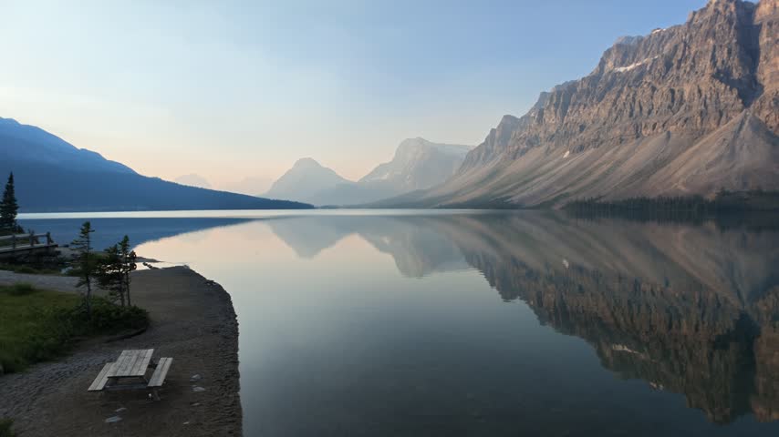 Beautiful Lake Bow reflecting the Rocky Mountains in calm turquoise water on a sunny summer day, with a clear blue sky in Banff National Park, Alberta, Canada.