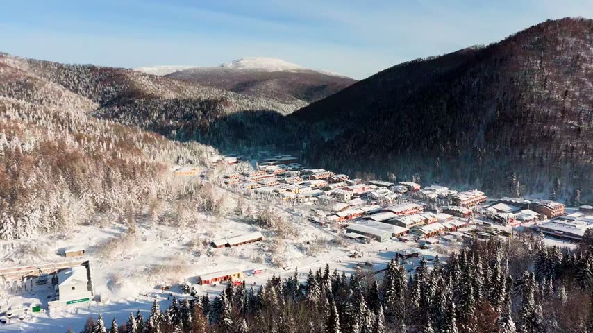 Xuexiang Snow Village In Valley Surrounded By Forested Mountains, Covered In Winter Snow In Heilongjiang, China. aerial panning shot