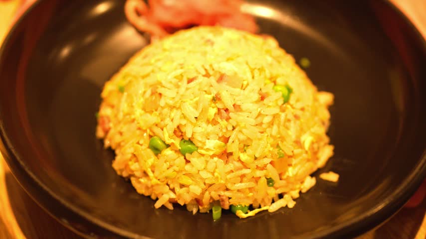 Japanese style egg fried rice chahan served on a black plate under warm restaurant lighting.