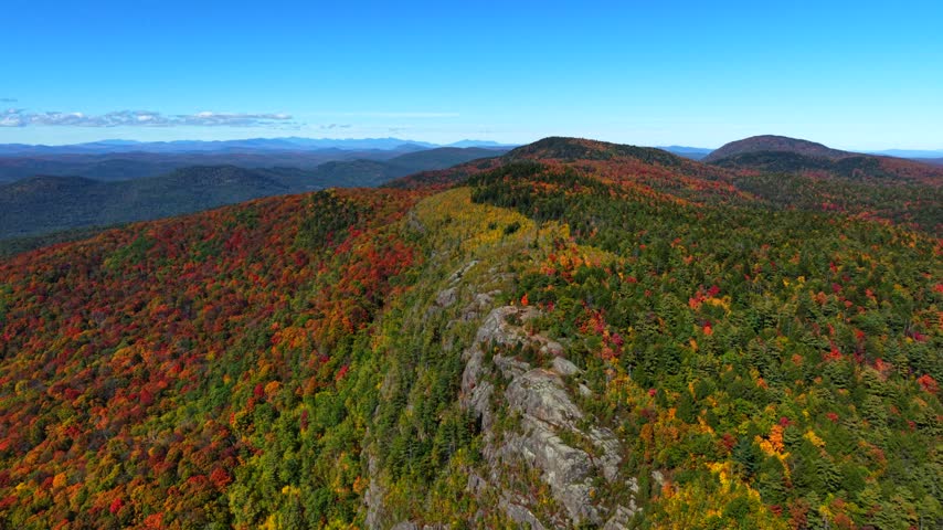 Vivid autumn trees blanket a rugged mountain ridge in the Adirondacks, New York wilderness