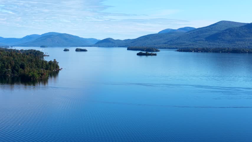Wide aerial view of calm lake with forested islands and distant Adirondack mountains