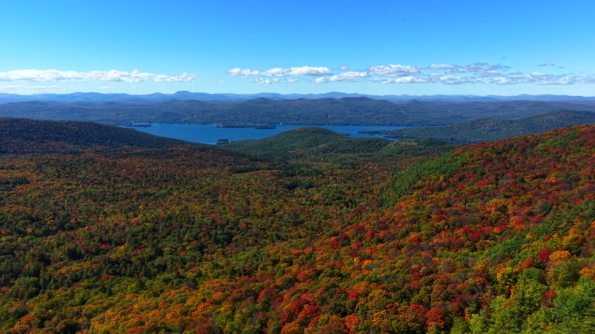 Aerial view of autumn forest and rocky summit overlooking lake and distant mountains