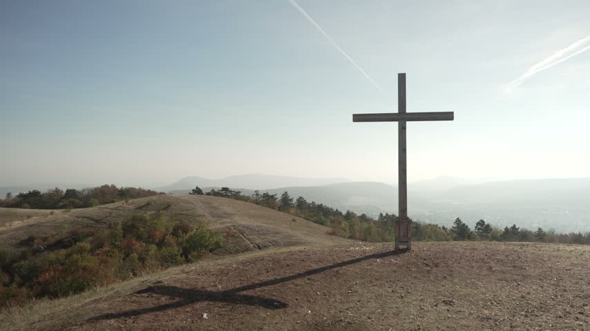 Wooden cross on a grassy summit overlooking a hazy landscape of distant ridges.