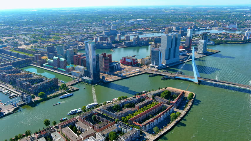 High-angle drone panorama of Rotterdam, Netherlands, showing Erasmus Bridge, the De Rotterdam skyscraper complex, Noordereiland and the Nieuwe Maas river lined with modern waterfront towers.