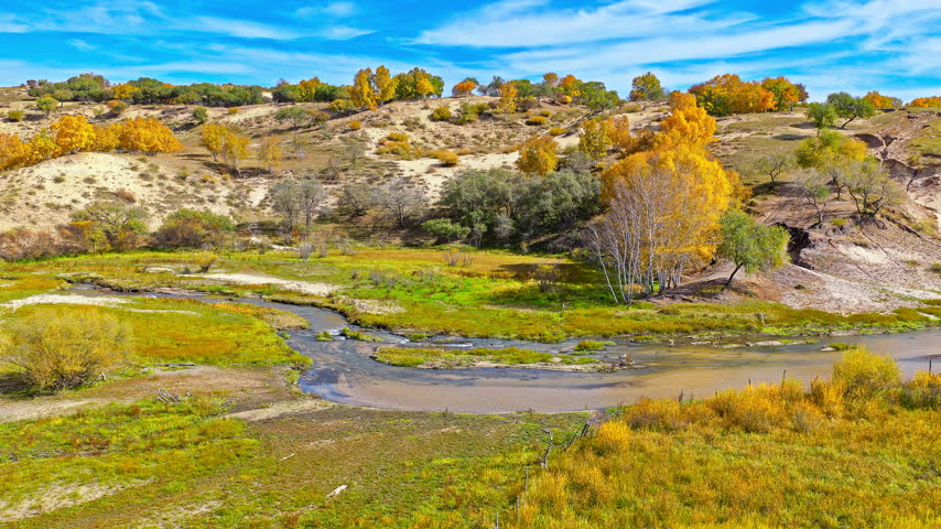 Scenic landscape of meandering river flowing through golden autumn grassland and hills in Inner Mongolia, China