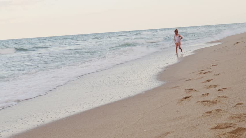Young child having fun running through shallow sea water and ocean waves near sandy shore