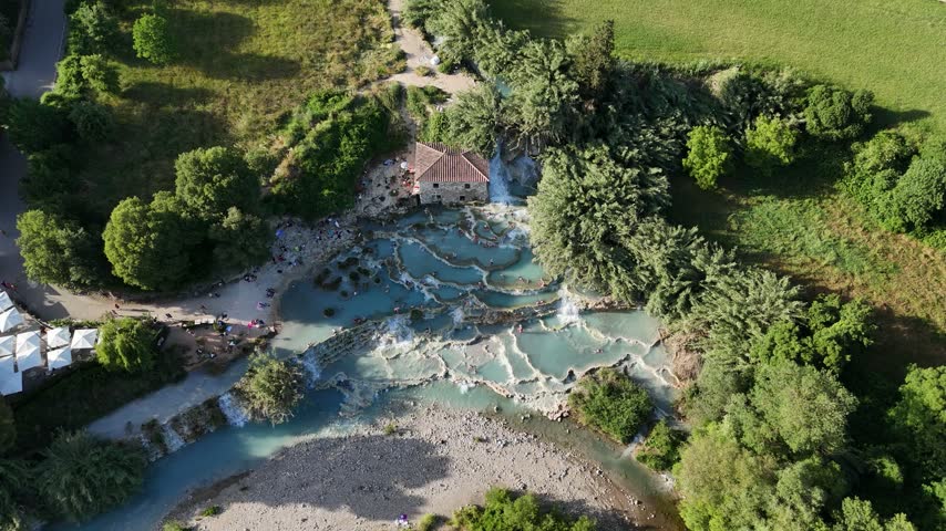 High angle drone shot capturing white water rushing down the natural travertine terraces of the Saturnia hot springs.
