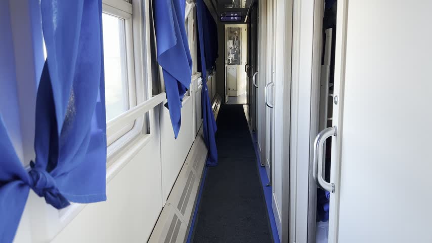 View down a narrow sleeper train corridor with blue curtains and open compartment doors