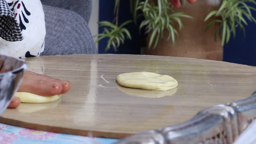 Hands spreading an oiled dough ball into a large thin sheet on a wooden board for Moroccan msemen trid