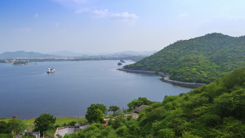Dense foreground foliage overlooks Fateh Sagar Lake and the road hugging its hillside shore in Udaipur.
