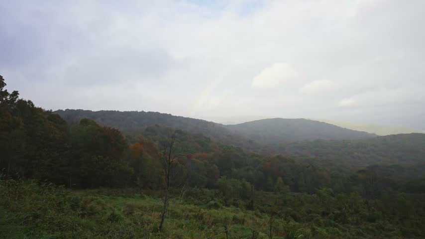 A faint rainbow arches over rolling autumnal mountain ridges and vast forest valleys at Grayson Highlands State Park.