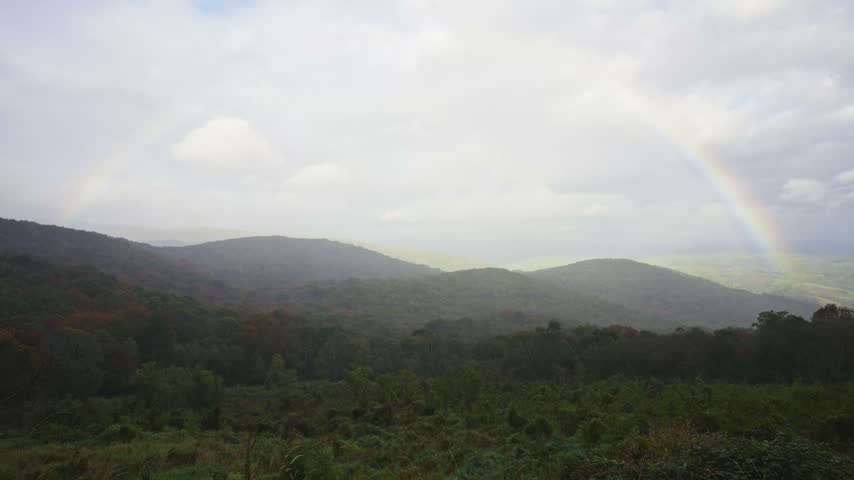 A faint rainbow arches over rolling autumnal mountain ridges and vast forest valleys at Grayson Highlands State Park.
