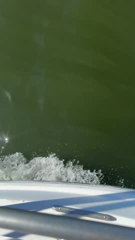 POV on a boat looking at the wake as the emerald water laps the side of the boat