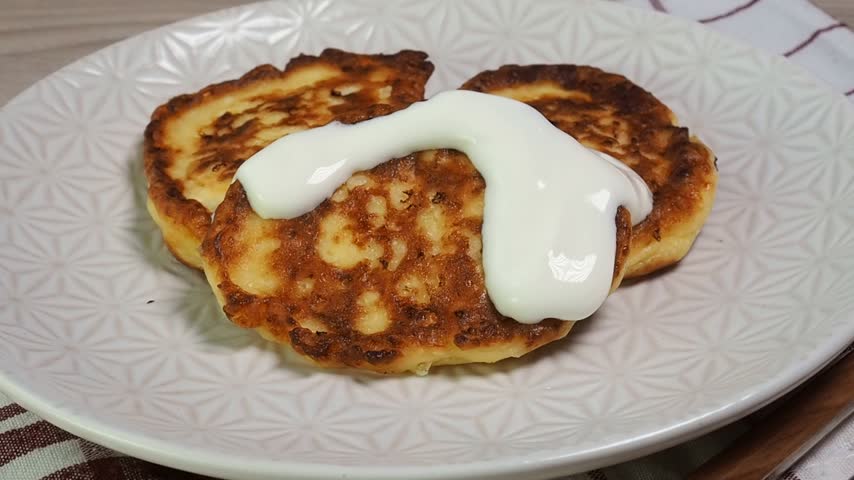 Cottage cheese pancakes on a plate are topped with sour cream. Fried cheesecakes with smetana.