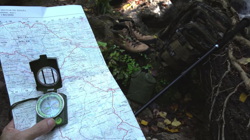 Hiking equipment lying on a riverbank beside a rushing mountain stream, tilting up to reveal lush green forest trees