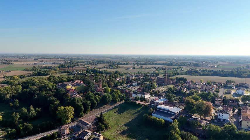Villa Castello Sforza Fogliani with towers and Chiesa di San Biagio campanile among trees above the Po Valley plain in Castelnuovo Fogliani, Alseno, Piacenza, Italy, drone forward flyover