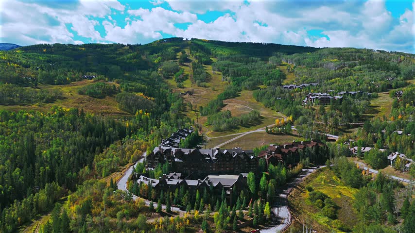 Aerial drone view of Beaver Creek Ski Resort ski trails lift sunny blue sky morning Fall Autumn Bachelor Gulch Vail Avon Colorado landscape Ritz Carton ski lodge buildings cars road windy backwards up