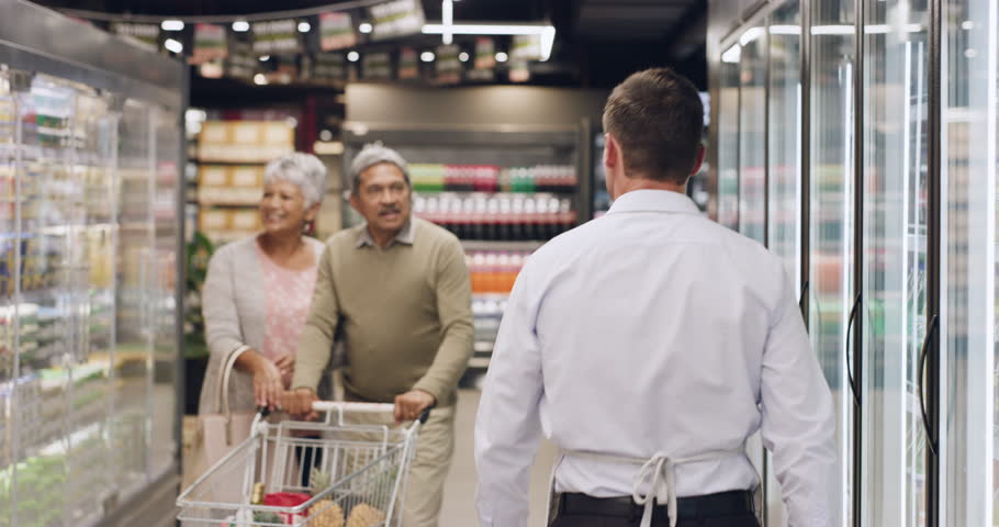 Old couple, grocery shopping and help with employee, question and search for diet options in store. Mature man, woman and customer in supermarket with fridge aisle for wellness, health and nutrition