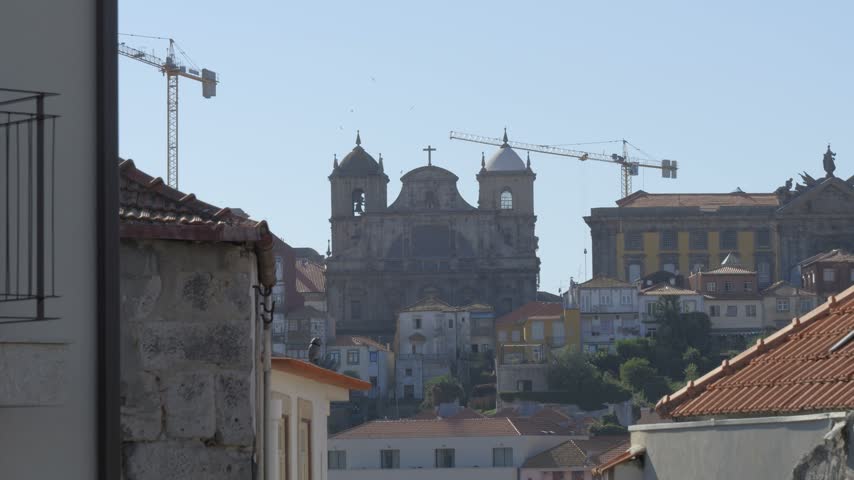Igreja de São Bento da Vitória rises above tiled rooftops in Porto, with construction cranes behind its twin bell towers.